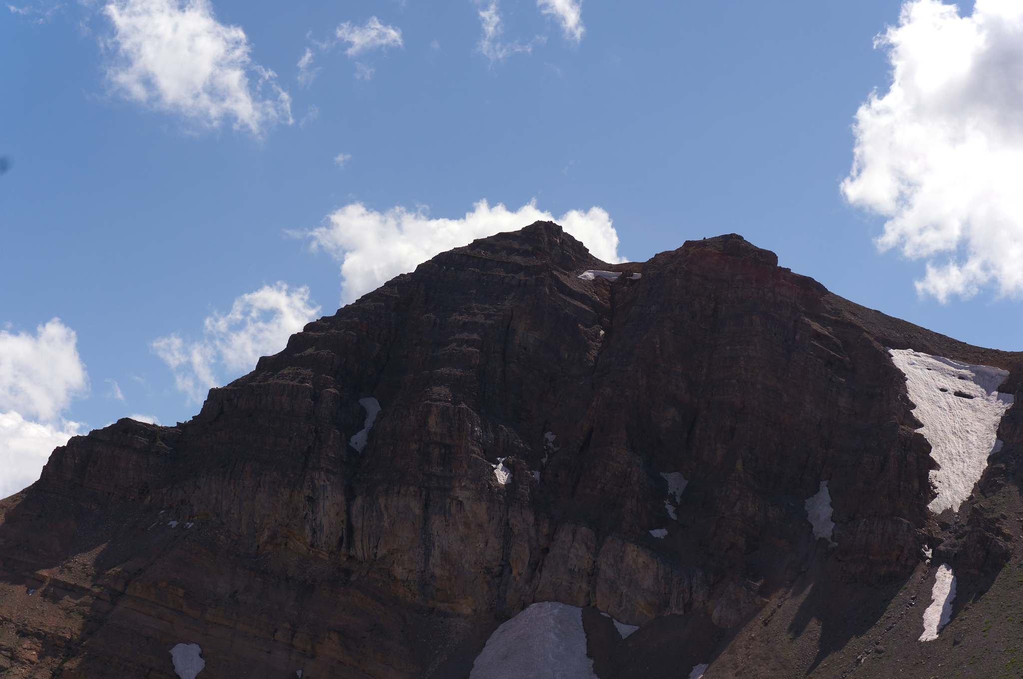 A mountain peak below a blue sky with scattered clouds.